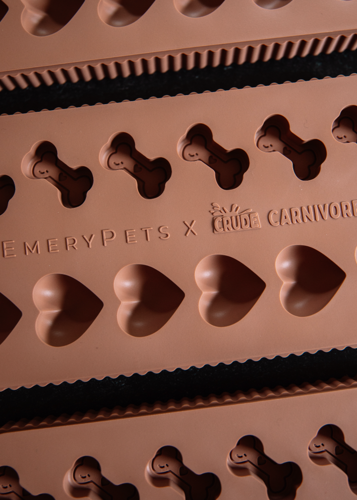 Silicone mold with bone and heart shapes branded 'EmeryPets x Crave Carnivore' on a dark surface.