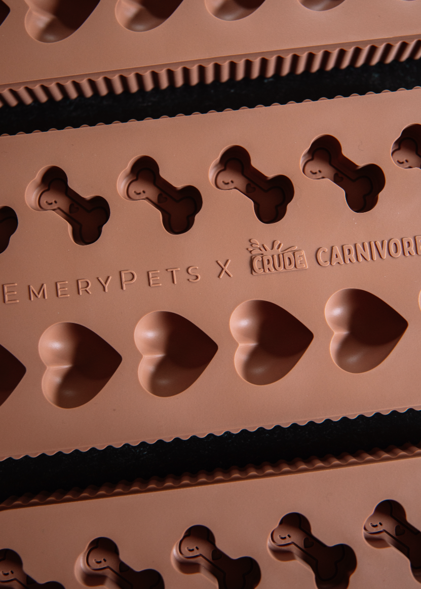 Silicone mold with bone and heart shapes branded 'EmeryPets x Crave Carnivore' on a dark surface.